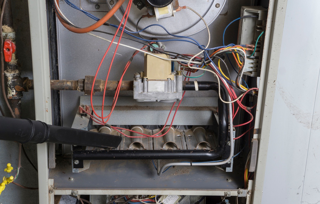 Technician vacuuming dust out of old furnace that is compromising air quality in the home